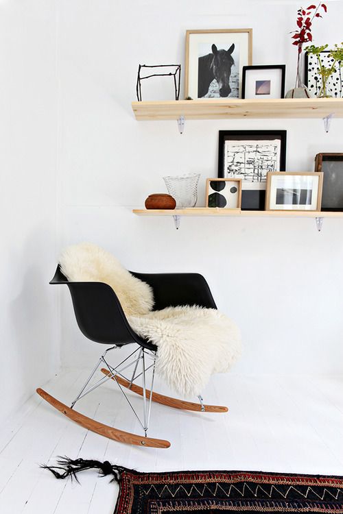a Scandinavian nook with a black Eames rocker, open shelves with decor and greenery and blooms plus a printed rug