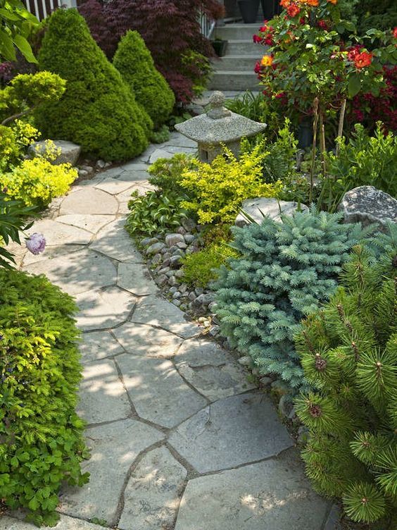 a Zen like garden with a stone garden path and greenery and shrubs lining it up, with a traditional stone Japanese lantern