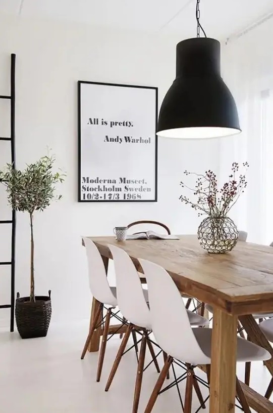 a beautiful Scandinavian dining room with a light-stained wooden table, white Eames chairs, a statement black pendant lamp and an artwork