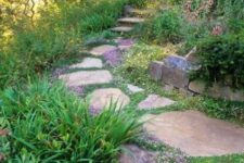 a beautiful and peaceful garden with a rough stone path, with greenery and purple blooms in between these stones, with plants around the path