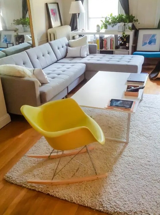 a beautiful living room with a dove grey sectional, a white coffee table and a yellow Eames rocker, potted greenery and a mirror