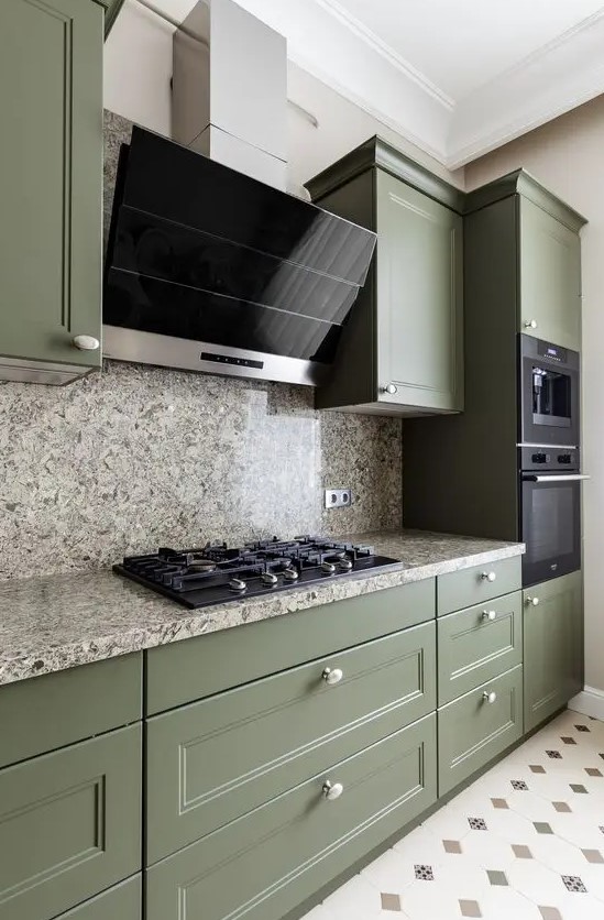 a beautiful olive green kitchen with shaker cabinets, grey stone countertops and a backsplash, black appliances