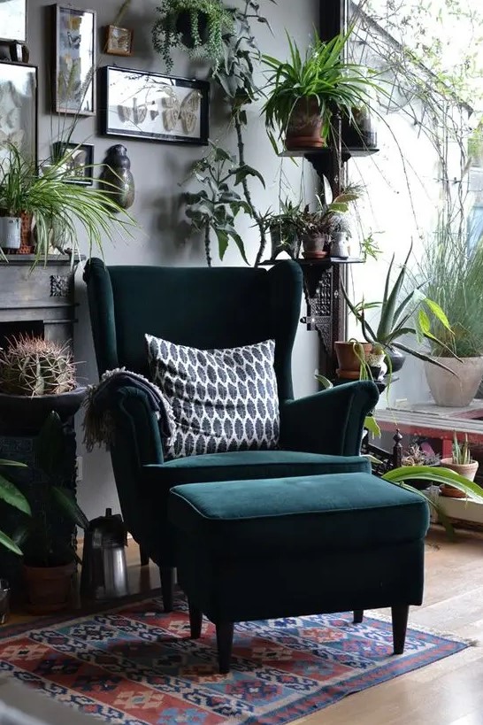 a bold boho nook with a dark green Strandmon wingback chair and a matching footrest, lots of greenery, cacti and artworks