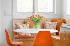 a bold dining corner with an upholstered bench, a round table, orange Eames chairs and a pendant lamp is cool