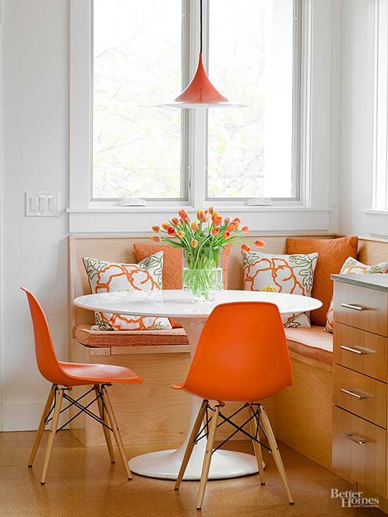 a bold dining corner with an upholstered bench, a round table, orange Eames chairs and a pendant lamp is cool