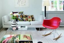 a bold living room with a white sofa, a colorful ottoman, a red Eames rocker, an acrylic coffee table and some books