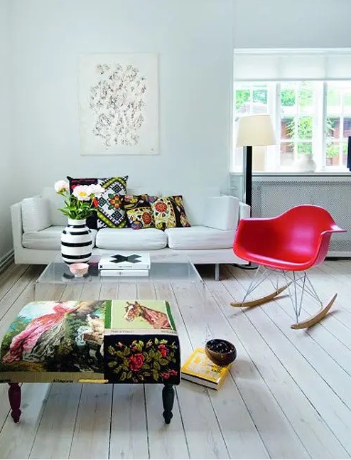 a bold living room with a white sofa, a colorful ottoman, a red Eames rocker, an acrylic coffee table and some books