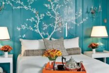 a bold turquoise bedroom with paneling on the walls, with a painted tree with leaves, a bed with neutral and grey bedding, white nightstands and turquoise and white table lamps