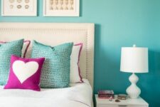a bright bedroom with a turquoise accent wall, a white bed and neutral bedding, a white nightstand and a lamp