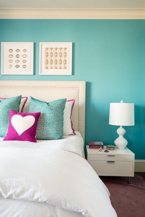 a bright bedroom with a turquoise accent wall, a white bed and neutral bedding, a white nightstand and a lamp