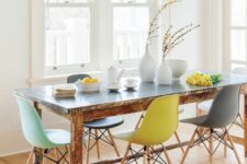 a bright dining room with a shabby chic dining table and colorful Eames chairs, a cage with bright birds and some decor