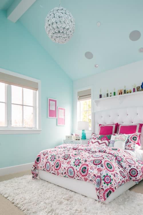 a bright teenage bedroom in light turquoise, with a bed and bold bedding, a shelving unit with decor