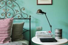 a catchy bedroom with a turquoise accent wall, a forged bed and a nightstand with a table lamp is welcoming