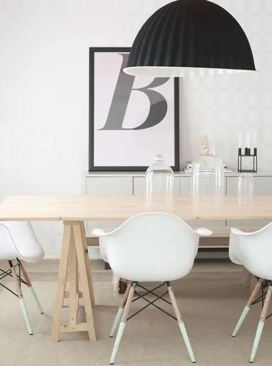 a catchy contrasting Scandinavian dining space with a long trestle table, white Eames chairs, a black pendant lamp and an artwork