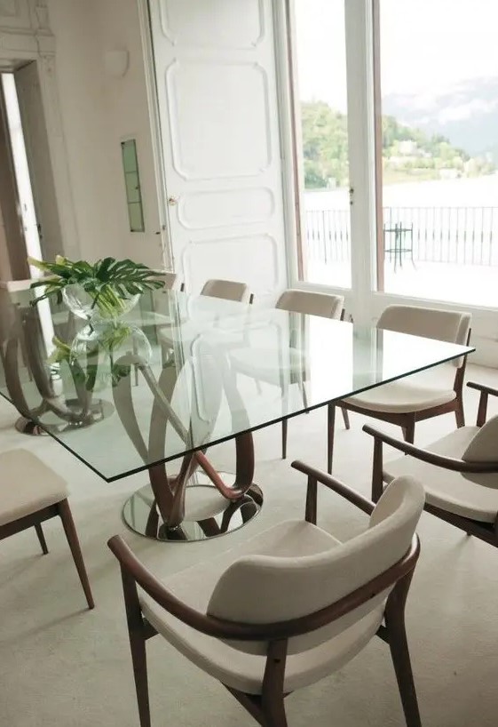 a catchy dining table with a glass tabletop and a rich-stained swirl base plus upholstered chairs and a lovely view for a perfect dining room