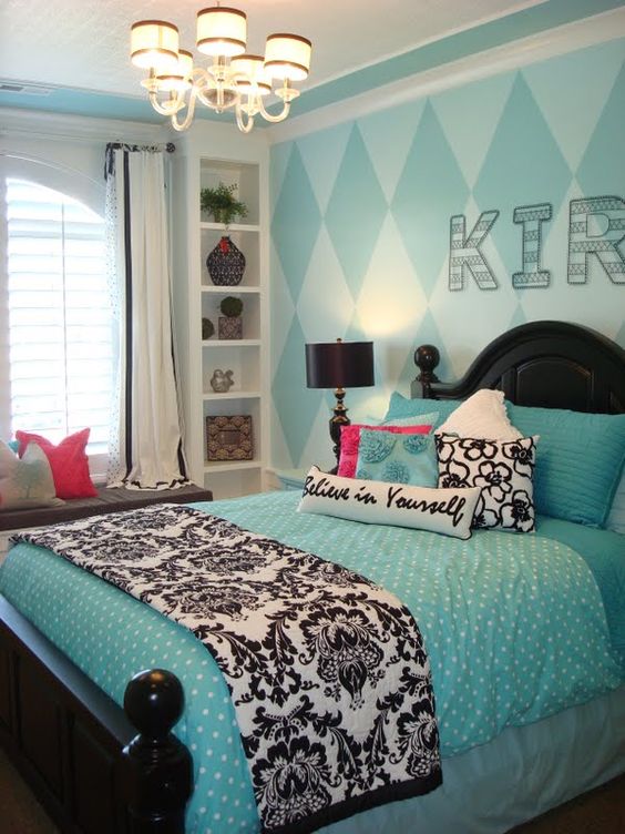 a catchy kid's room with an accent turquoise geo wall, a black bed with turquoise bedding, a shelving unit and a windowsill bench