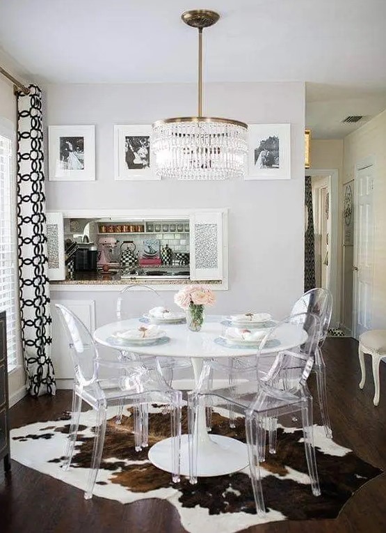 a catchy modern farmhouse dining space with a round table, ghost chairs, a cowhide rug, a crystal chandelier and a gallery wall