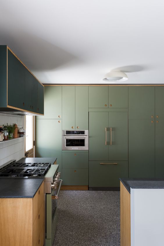 a catchy olive green kichen with sleek cabinets, brass handles and stained lower cabinets, black countertops