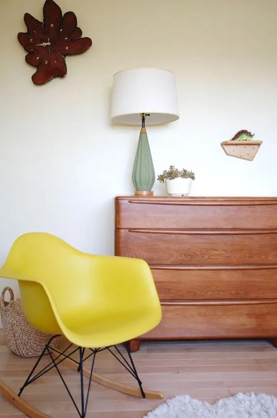 a catchy space with a rich stained dresser, a yellow Eames rocker, a table lamp, a quirky clock and a basket
