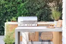 a chic contemporary bbq area of wood and concrete, with a grill and a cooking zone, a concrete dining area and rattan stools