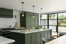 a chic contemporary kitchen with dark olive green cabinets, white countertops, a black cooker and bulbs over the kitchen island