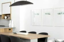 a chic minimalist dining space with a concrete and wood table, black chairs, a black pendant lamp and a minimalist gallery wall