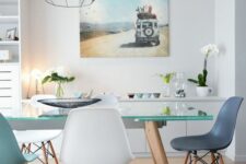 a coastal dining space with white storage units, a glass dining table, blue and white Eames chairs and a geometric pendant lamp
