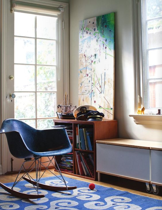 a colorful nook with a minimal credenza, a bookshelf, a bold artwork and a rug and a bold blue chair is a stylish space