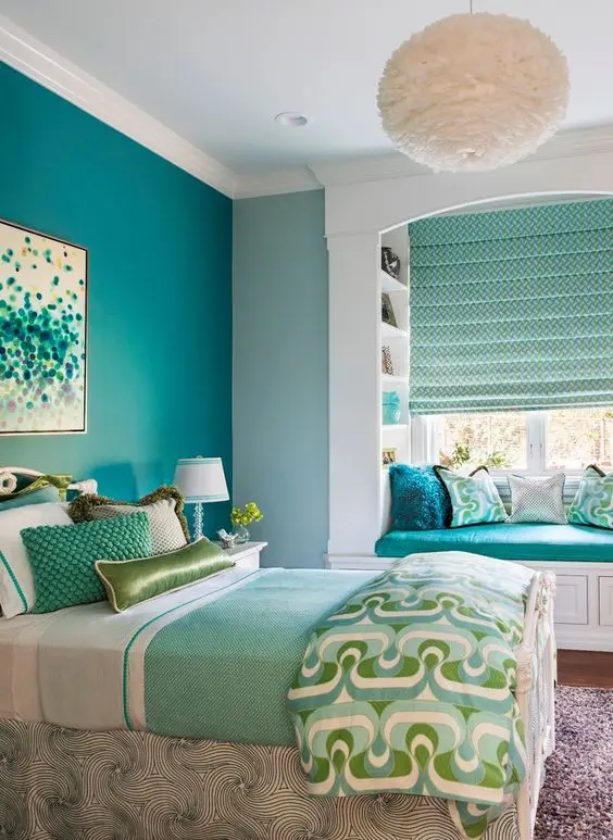 a colorful teen girl room with a turquoise accent wall, a bed with colorful and printed bedding, a windowsill seat and curtains