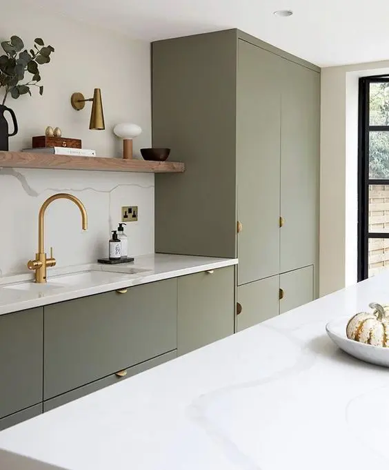 a contemporary olive green kitchen with sleek cabinets, gold pulls and a faucet, an open shelf and greenery