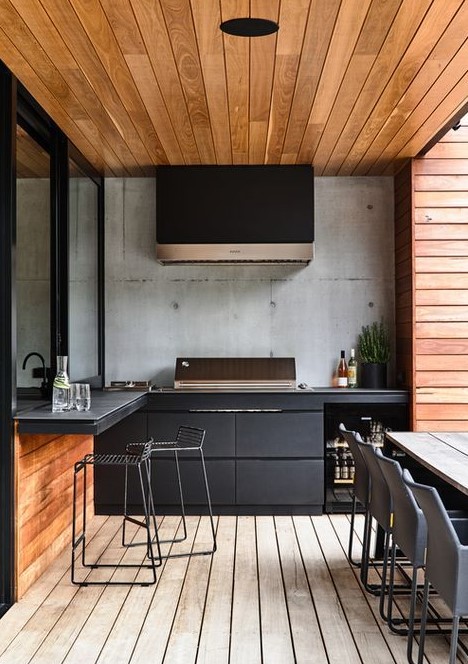 a contemporary outdoor barbecue area done in black and stained wood, with matte cabinets, a grill, a hood and some meal spaces