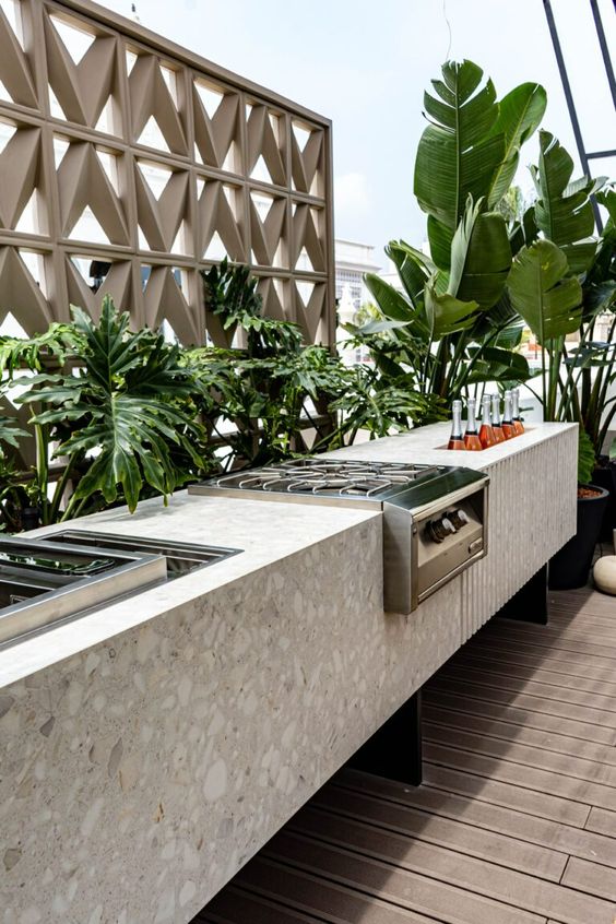 a contemporary outdoor bbq area with a large terrazzo slab piece with a grill, cooker and a wine storage niche plus greenery that lines it up