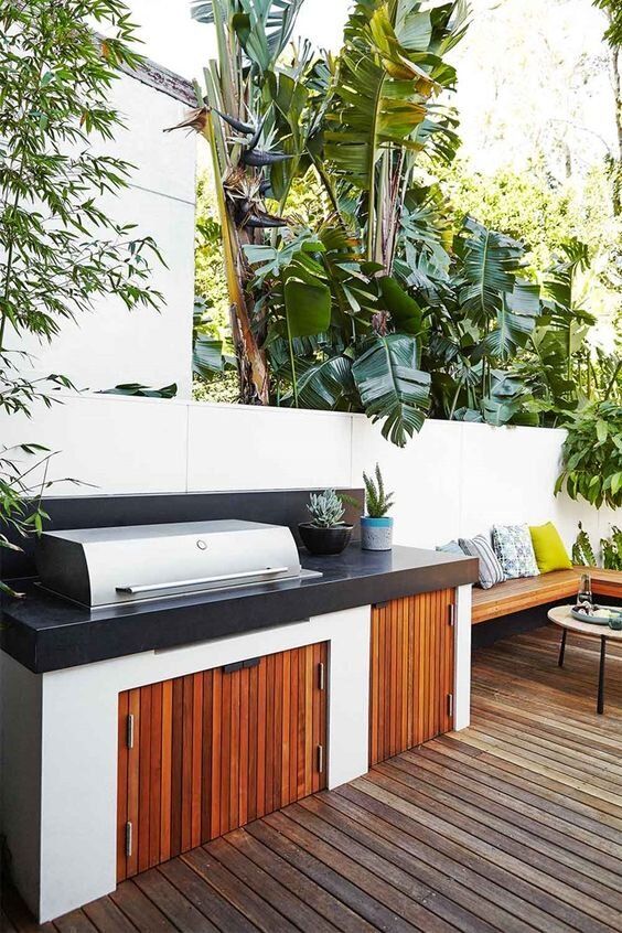 a contemporary outdoor bbq area with a wooden deck, a wall-mounted wooden bench, a concrete and wood cabinet with a grill