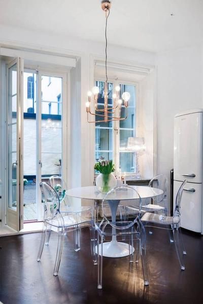 a cool and small dining space with a round table, ghost chairs, a catchy chandelier and an entrance to the balcony