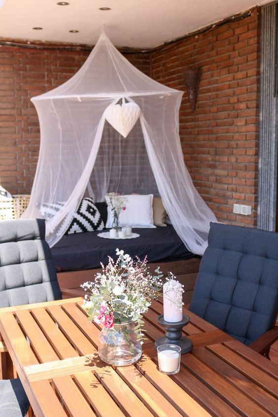 a cool balcony with a crate table and upholstered chairs, a pallet seat with upholstery and pillows, a mosquito net canopy