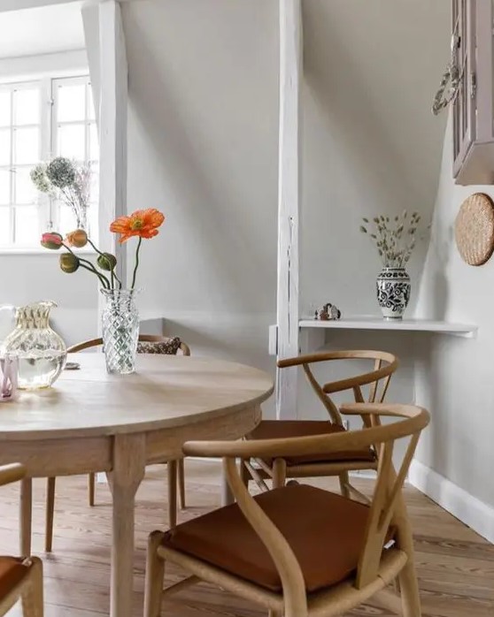 a cool dining space with a round stained table and wishbone chairs, some decor and a storage cabinet on the wall