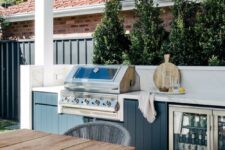 a cool outdoor grill area with a large fluted cabinet with a uilt-in grill and fridge, with a small dining zone