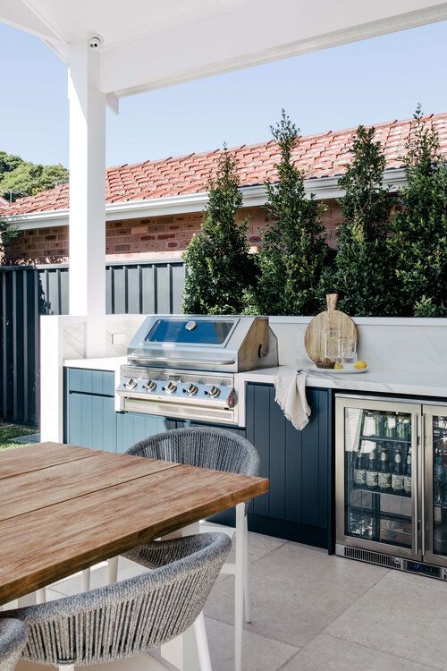 a cool outdoor grill area with a large fluted cabinet with a uilt-in grill and fridge, with a small dining zone
