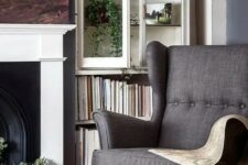 a cozy and welcoming living room with a fireplace, bookshelves, a cabinet with greenery, a grey Strandmon chair