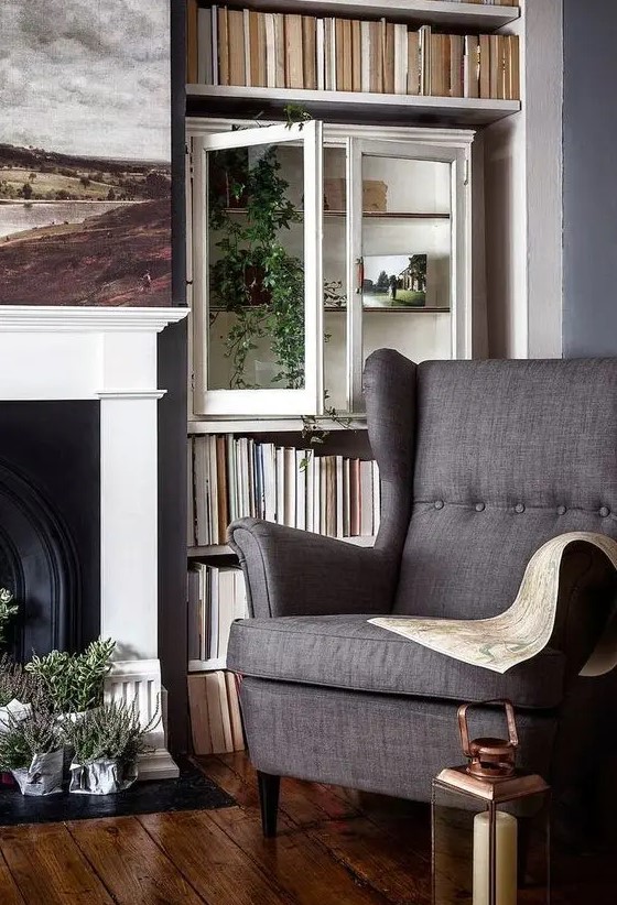 a cozy and welcoming living room with a fireplace, bookshelves, a cabinet with greenery, a grey Strandmon chair