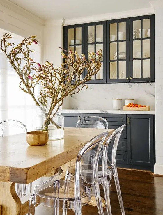 a cozy farmhouse dining room with graphite grey built-in cabinets, a white marble backsplash, a stained table and ghost chairs