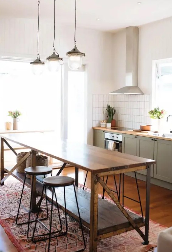 a cozy mid-century modern kitchen with lower olive green cabinets, a vintage wooden kitchen island, wooden stools and vintage pendant lamps