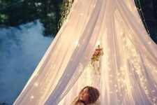 a cozy outdoor space of some blankets and pillows and a mosquito canopy with lights over it is a fairy-tale idea