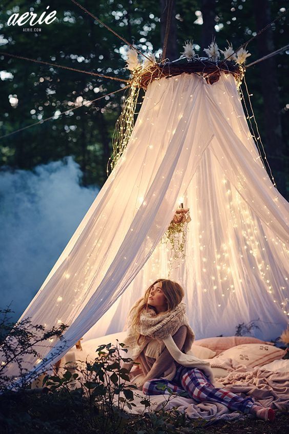 a cozy outdoor space of some blankets and pillows and a mosquito canopy with lights over it is a fairy tale idea