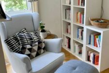 a cozy reading nook with a bookshelf, a white Strandmon chair, a grey footrest, a floor lamp and printed pillows