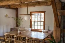 a cozy rustic dining space with stained wooden beams, a built-in bench, a stained table and chairs, a lovely pendant lamp and greenery