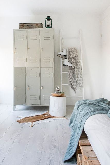 a creative neutral bedroom with a pallet bed and neutral and blue bedding, a stack of grey lockers, a ladder, a whitewashed stump and some vintage decor