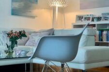 a delicate living room with a white sectional, a white Eames rocker, a glass coffee table and some pastel artwork