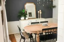 a farmhouse dining room with a grey accent wall, a vintage wooden dining table, black chairs and a bench, a vintage chandelier and a sideboard with some decor