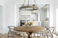 a farmhouse dining space with a large wooden dining table and grey wishbone chairs, a heavy round chandelier is cool and cozy